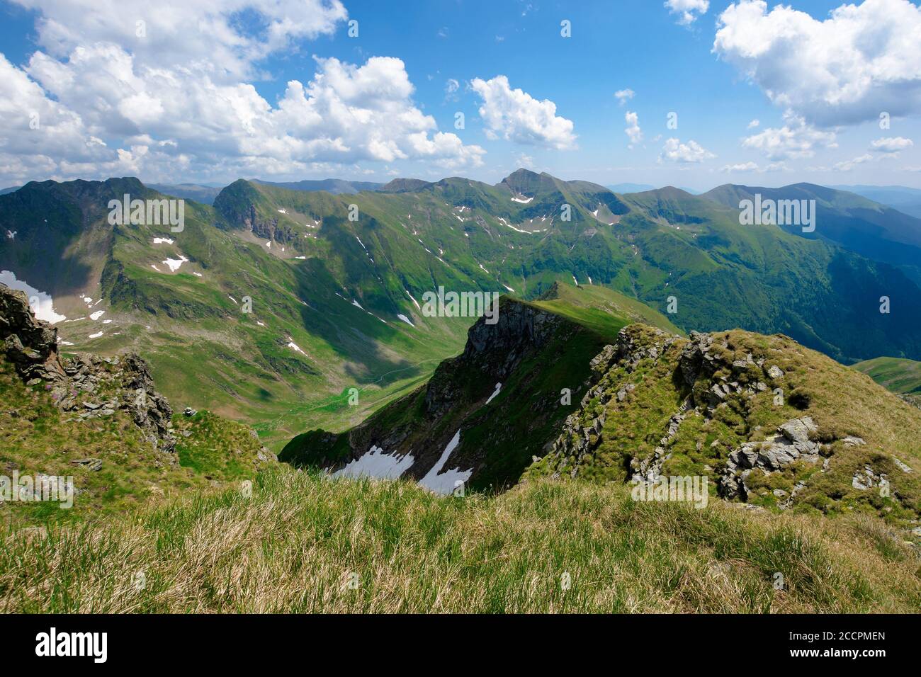 Bergkulisse von rumänien im Sommer. Gras auf den Wiesen und im Tal. Felsen und Schnee an den steilen Hängen. Wolken am Himmel. Sonniges Wetter Stockfoto