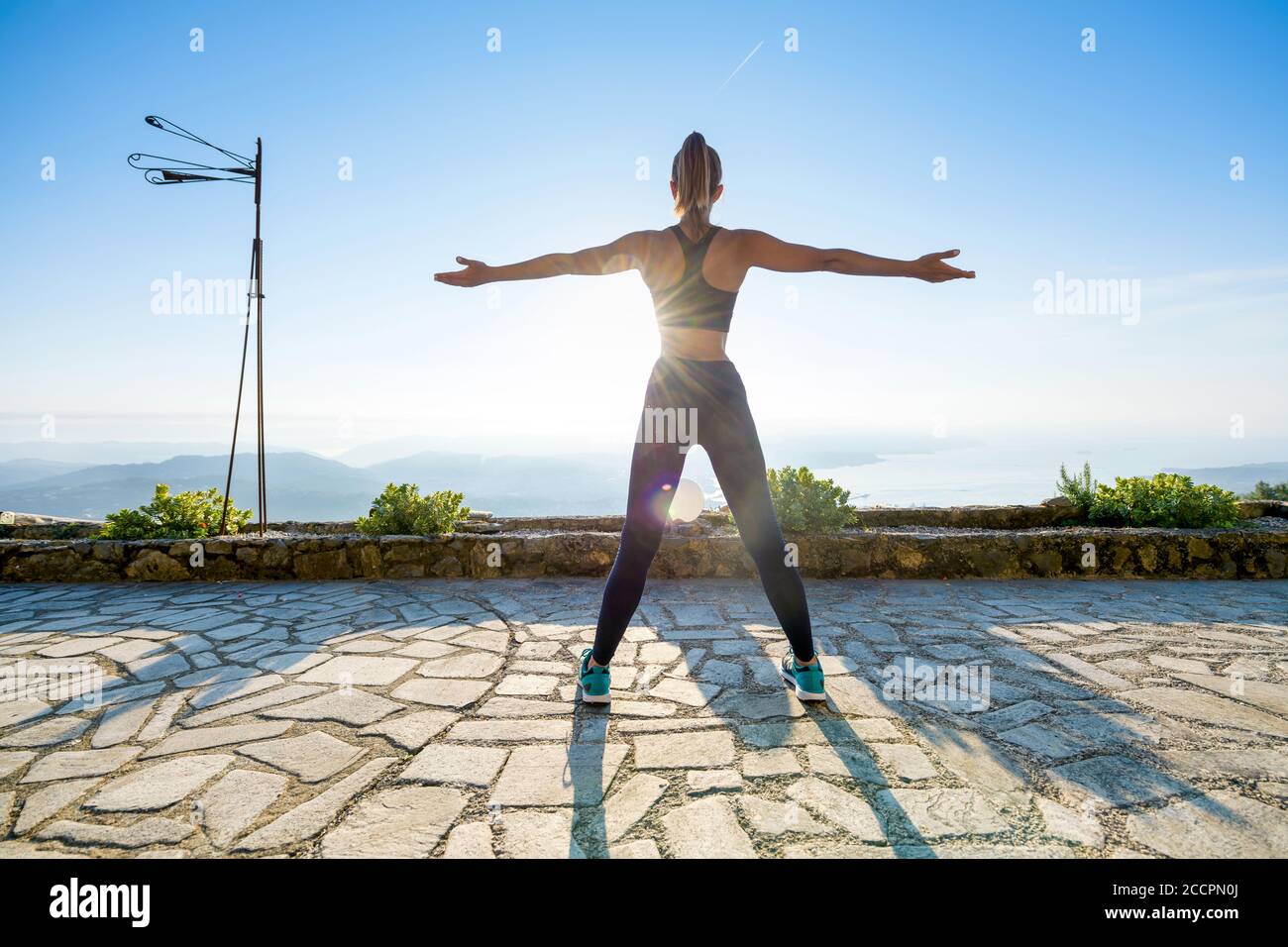 Fit muskulösen Mädchen beim Sonnenaufgang auf einem Stein zu arbeiten Terrasse mit Blick auf die aufgehende Sonne mit ausgestreckten Armen im Freien Der Garten in der Gesundheit und der Fitness Stockfoto