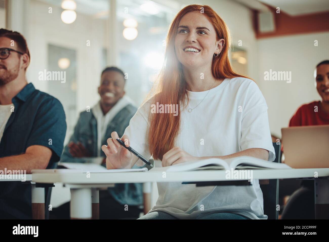 Hübsche Studentin, die in der Vorlesung aufpasst. Mädchen, die dem Lehrer zuhören und lächeln im Klassenzimmer sitzen. Stockfoto