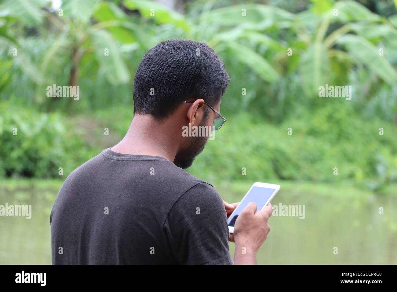 Junger Mann mit Smartphone und Blick auf den Handy-Bildschirm, von der Rückseite genommen Stockfoto