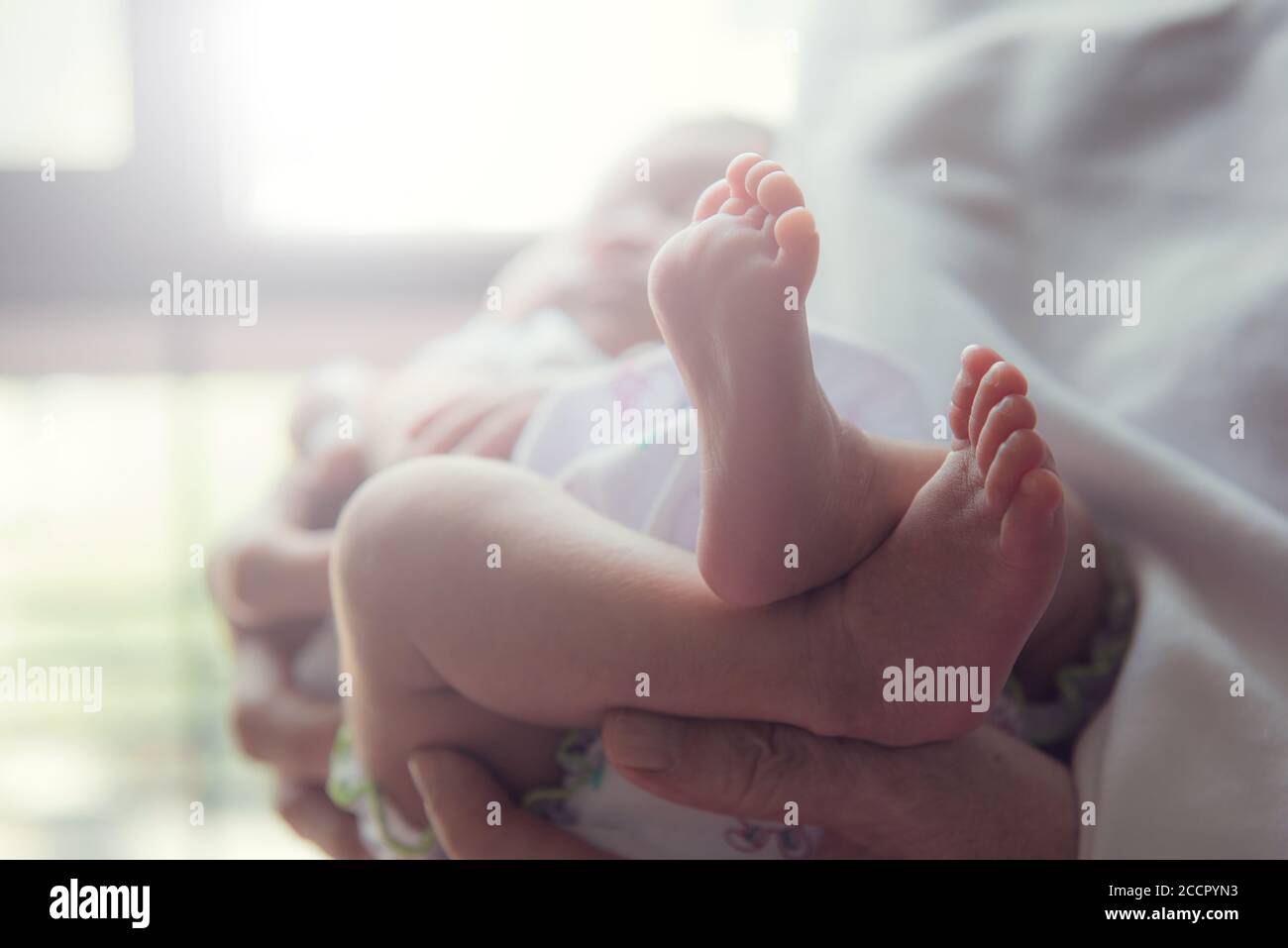 Elternteil hält kleines Kleinkind. Der Fuß des Babys ist im Fokus. Stockfoto