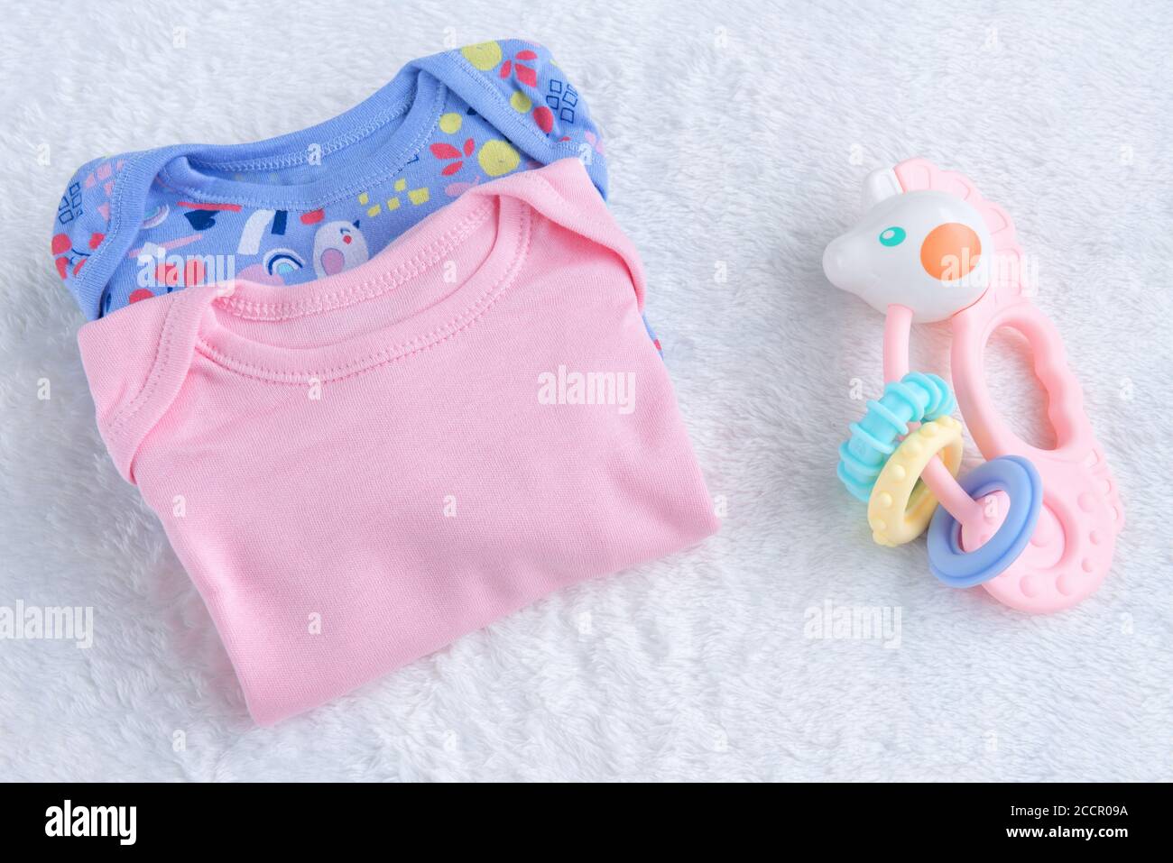 Babymockup. Bodysuits für Baby Mädchen und Rassel Spielzeug auf EINEM weißen Pelz Teppich. Konzept Für Neugeborene. Baby Mädchen Kleidung Set. Stockfoto