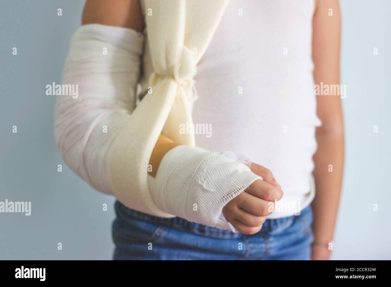 Kleines Mädchen mit gebrochener Hand, in Gips, gegen blaue Wand Stockfoto