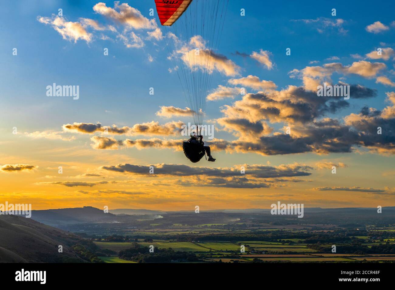 Gleitschirm, der gegen die untergehende Sonne und vereinzelte Wolken fliegt, über dem South Downs National Park. Brighton, East Sussex. Vereinigtes Königreich Stockfoto