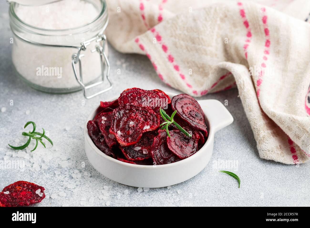 Gesunde Bio Purple Baked Beet (Rote Bete) Chips mit Olivenöl, großem Meersalz und Rosmarin in einer weißen Schüssel auf grauem Betongrund. Diätetisch Stockfoto