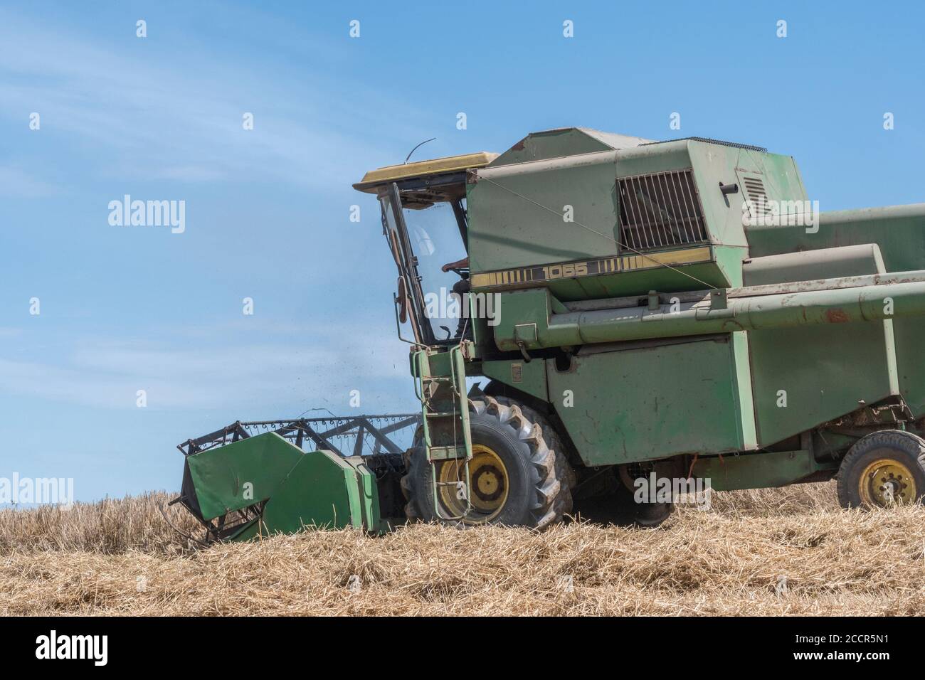 John Deere Mähdrescher Schneiden Weizenernte in der Sommersonne. Vorderer Schneidwerkkopf, Zinkenrolle und Seitenrohr sichtbar. Für 2020 UK Weizenfeld Ernte. Stockfoto