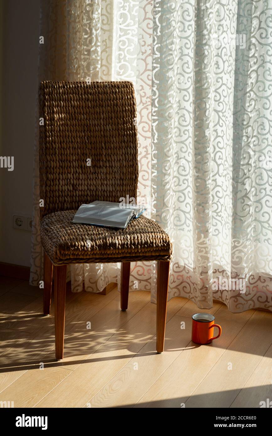 Innenausstattung mit Korbsessel, Vorhängen, Buch und Morgenkaffee. Design-Wohneinrichtung. Sonniger Morgen. Böhmisches Konzept. Stockfoto