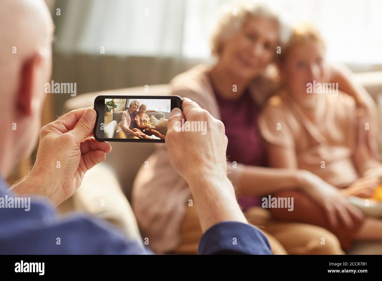 Porträt eines älteren Mannes, der Smartphone-Foto von Frau und Enkelin für Familienerinnerungen macht, Fokus auf Smartphone-Bildschirm, Kopierraum Stockfoto