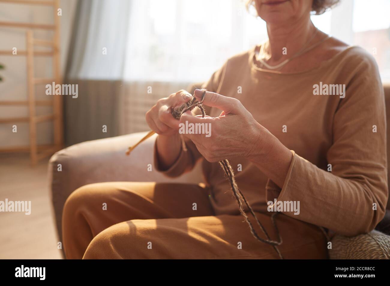 Warm getönte Nahaufnahme von nicht erkennbaren Senior Frau Stricken in gemütlichen Zuhause Innenraum durch Sonnenlicht beleuchtet, kopieren Raum Stockfoto