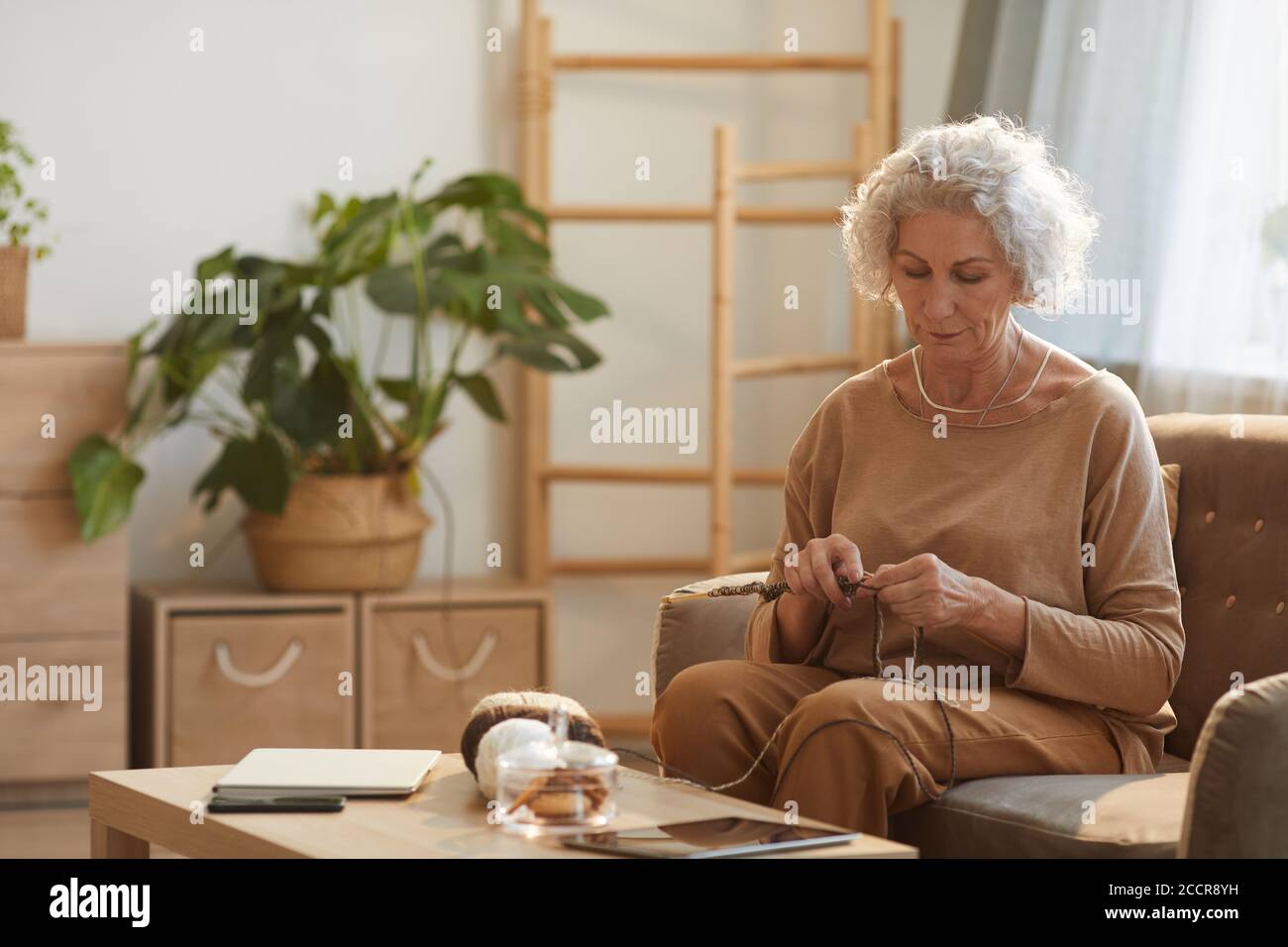 Warm getönte Porträt des Inhalts Senior Frau Stricken in gemütlichen Hause durch Sonnenlicht beleuchtet, kopieren Raum Stockfoto