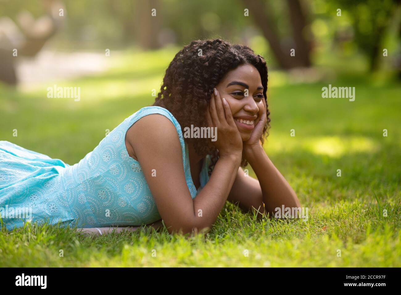 Schöne schwarze Dame in blauem Kleid entspannend auf Gras an Sommerpark Stockfoto