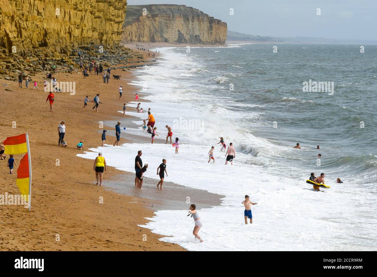 West Bay, Dorset, Großbritannien. August 2020. Wetter in Großbritannien. Urlauber und Sonnenanbeter am Strand genießen an einem luftigen Nachmittag mit warmem Sonnenschein ein Bad im rauhen Meer im Badeort West Bay in Dorset. Bild: Graham Hunt/Alamy Live News Stockfoto