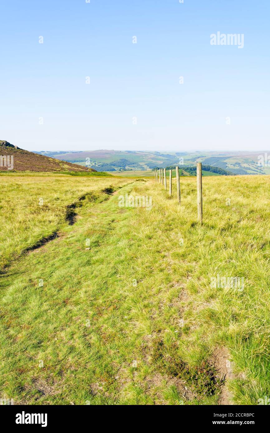 Eine Linie aus hölzernen Zaunpfosten an der Seite eines kaum sichtbaren Fußwegs im Derbyshire Peak District Stockfoto