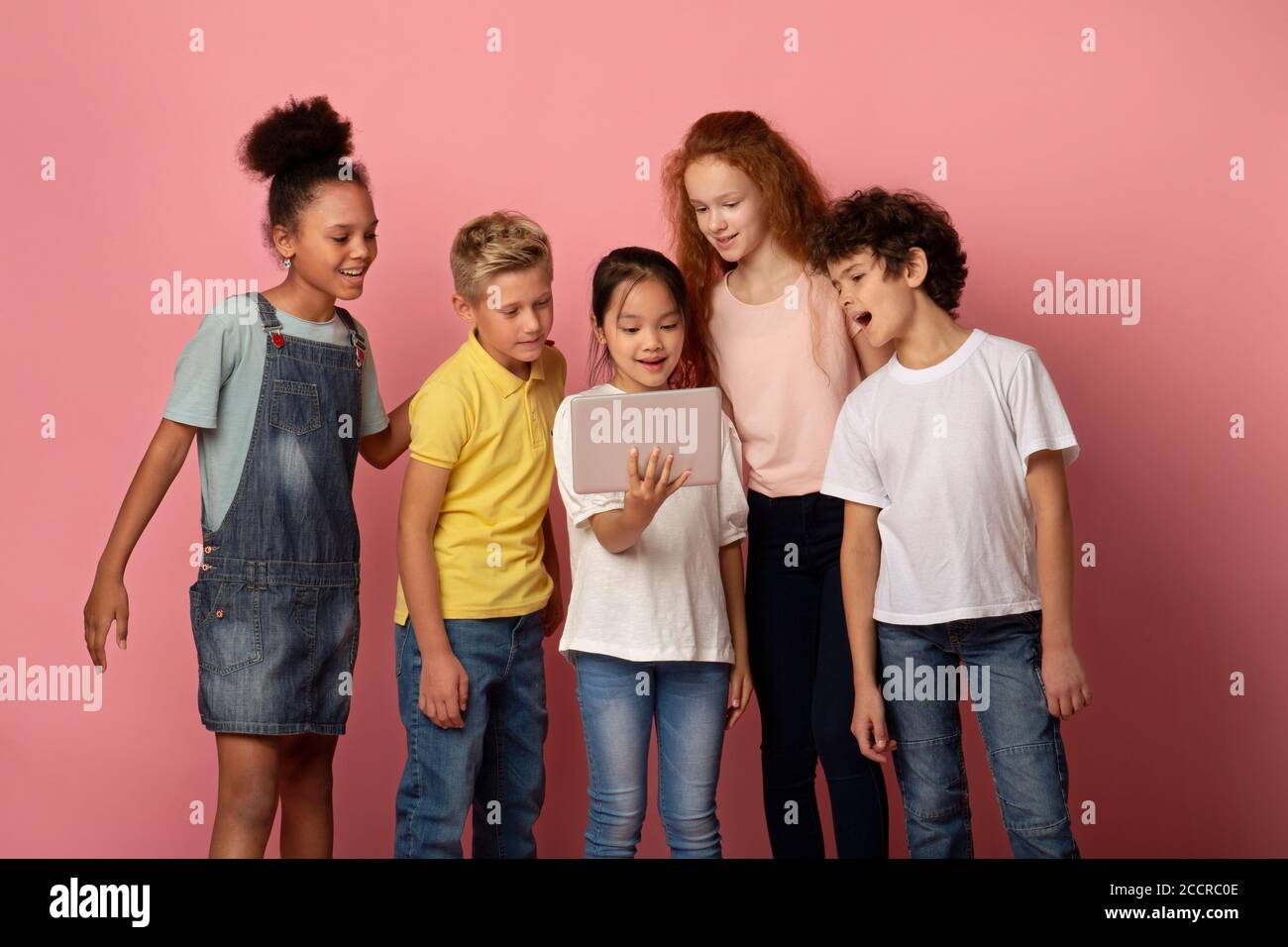 Online-Schulung. Glückliche Kinder beobachten interessante Web-Lektion auf Tablet-Computer über rosa Hintergrund Stockfoto
