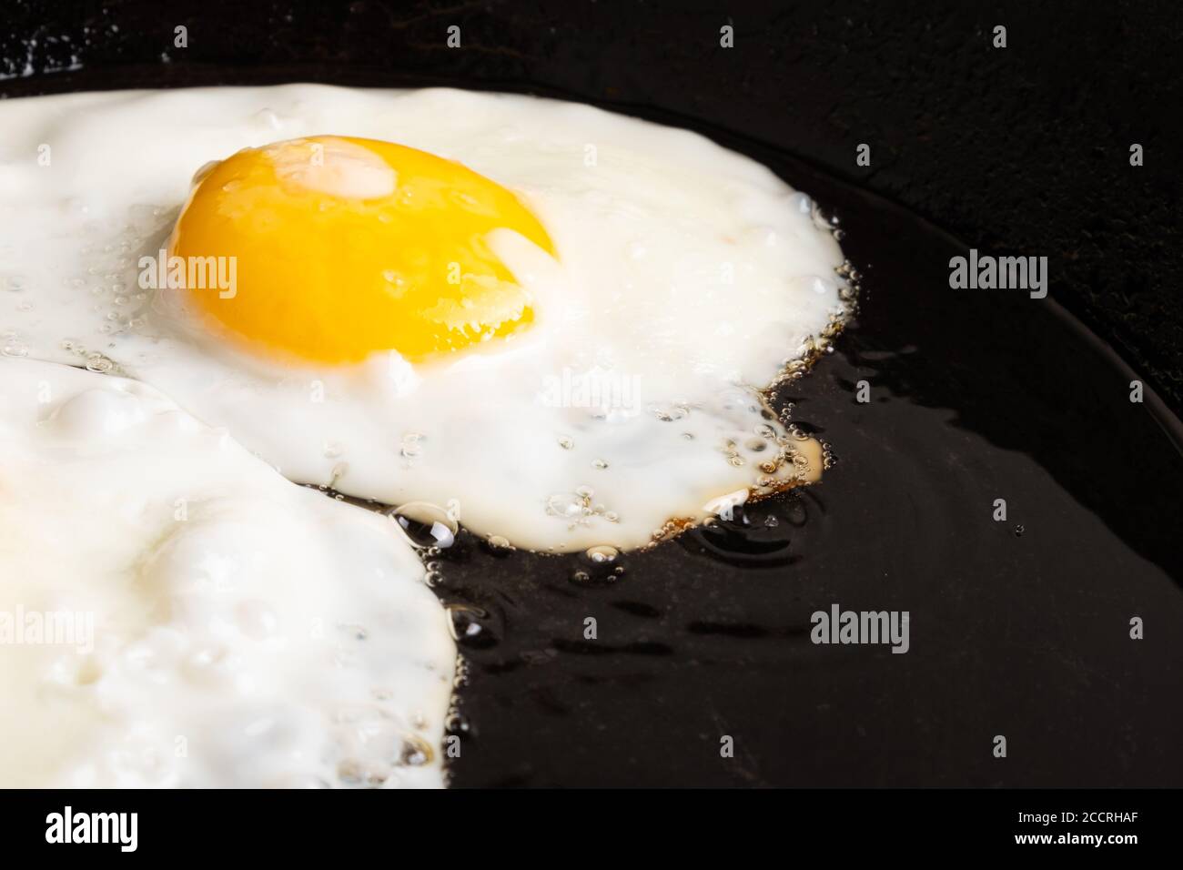 Gebratenes Hühnerei in einer schwarzen gusseisernen Pfanne aus nächster Nähe, Frühstück. Stockfoto