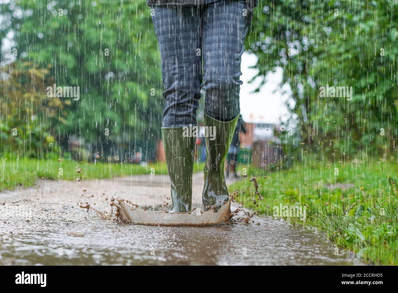 Nahaufnahme, Vorderansicht der grünen Gummistiefel, die von einer Frau getragen werden, die bei starkem Regen in Großbritannien durch Pfützen spritzt. Stockfoto