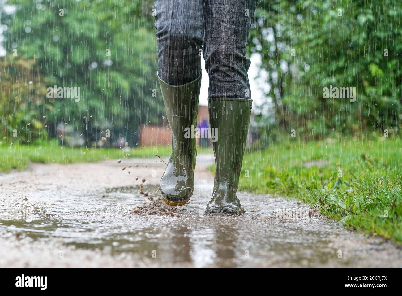 In der Nähe, Vorderansicht der grünen Gummistiefel, die von einer Frau im Freien getragen werden, die bei starkem Regen durch Pfützen spritzt, Großbritannien. Stockfoto