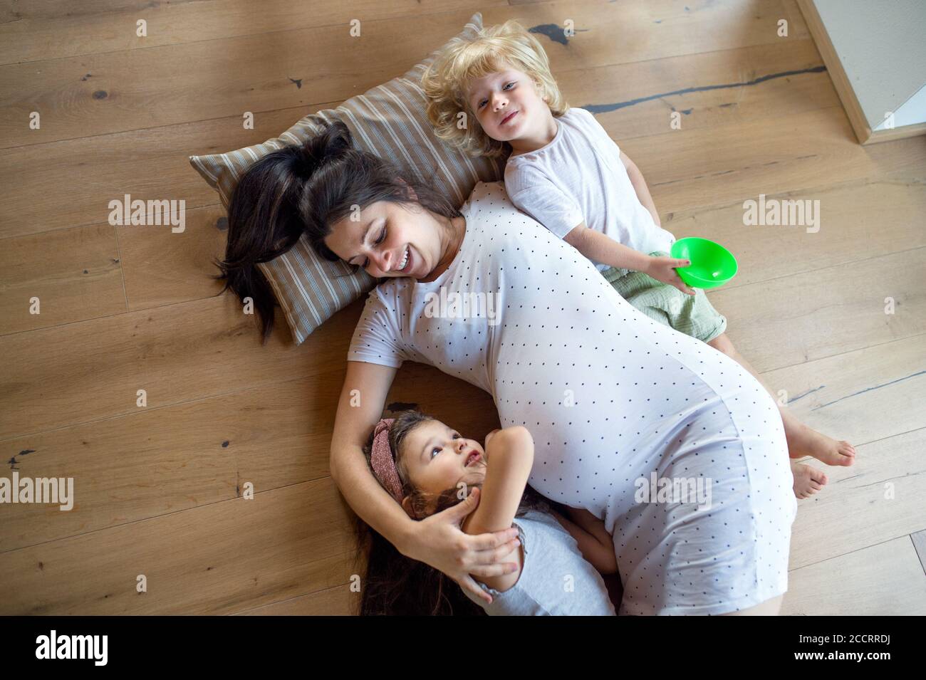 Draufsicht auf schwangere Frau mit kleinen Kindern zuhause, auf dem Boden liegend. Stockfoto