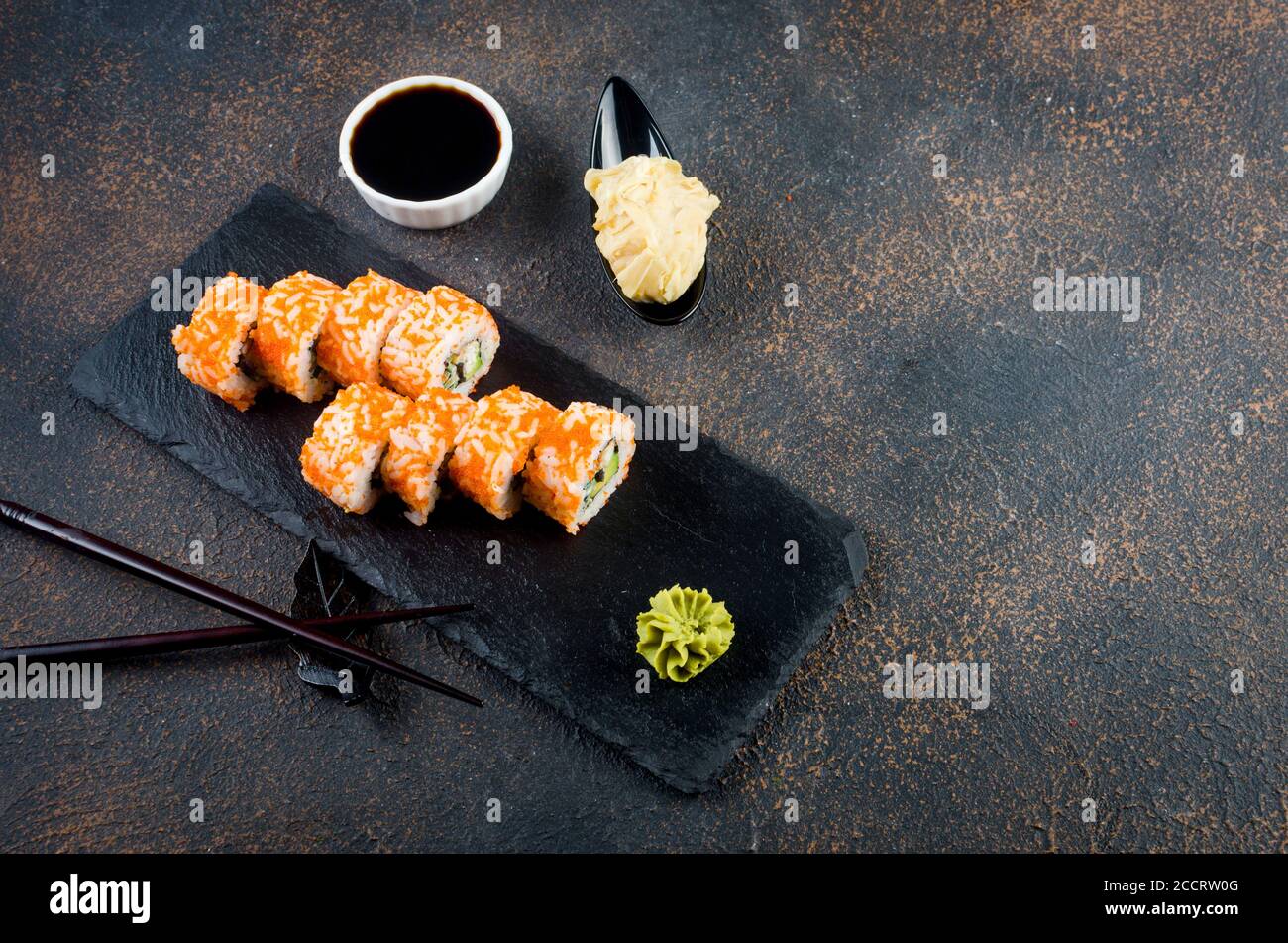 Maki-Brötchen auf Steinplatte mit Soßen, Ingwer und Wasabi Stockfoto
