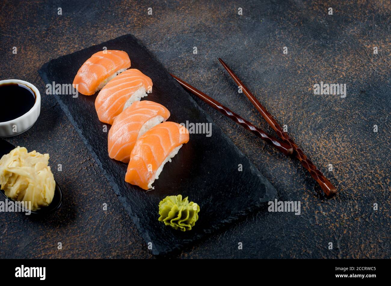 Leckeres Nigiri Sushi mit Lachs auf schwarzem Steinteller mit Sojasoße, Ingwer, Wasabi Stockfoto