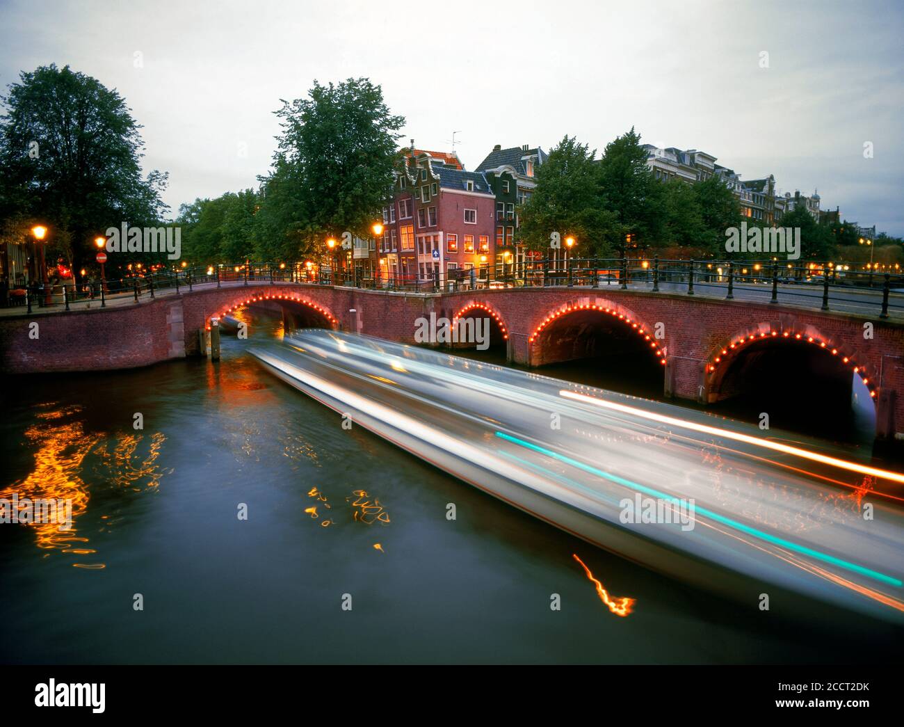 Boote, die durch die Kanäle und unter Straßenbögen von Amsterdam in der Abenddämmerung Stockfoto