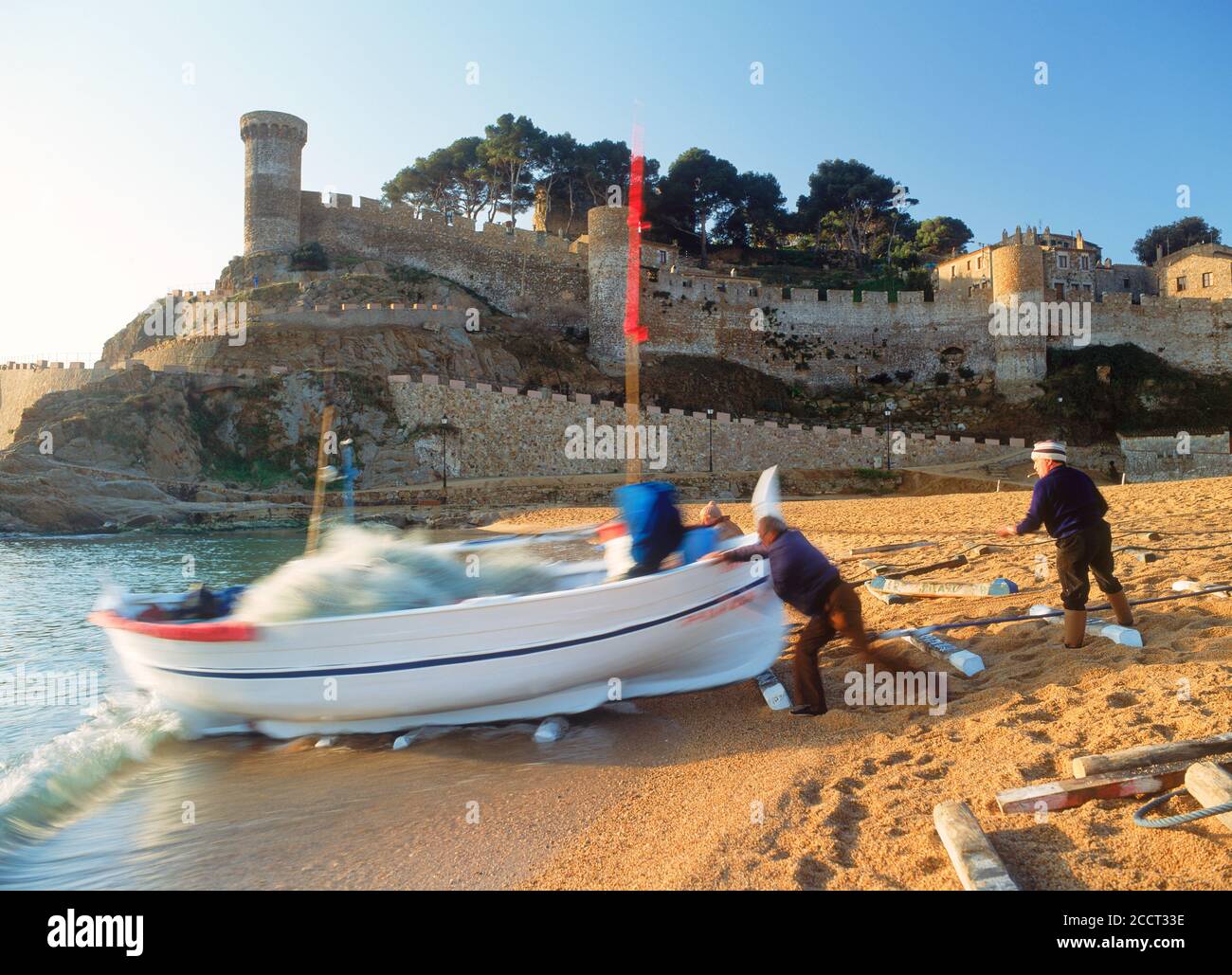 Fischer schieben Boot in Uferwellen auf Tossa De Mar Strand in Girona Provinz Spanien bei Sonnenaufgang Stockfoto