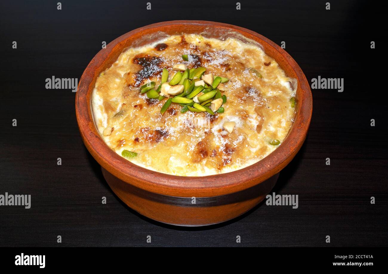 Traditionelles arabisches, östliches Dessert Om Ali. Draufsicht. Ägyptisches Brot Pudding in einer braunen Schale auf dunklem Holztisch, Nahaufnahme. Ägypten süß gebackenes Gebäck Stockfoto