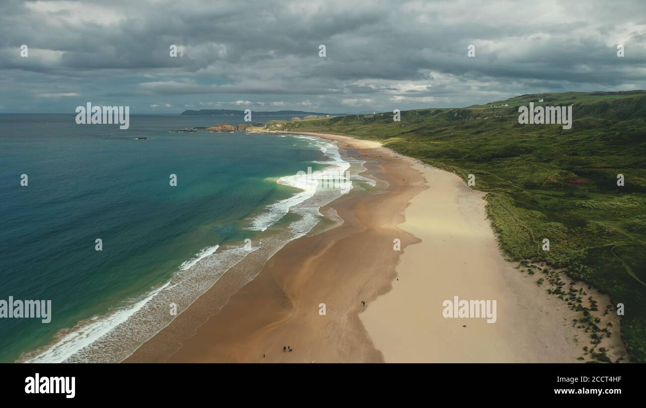 Nordirland Luftaufnahme: White Beach Golf Wasser stürzt ab. Die Leute am Ufer laufen und spielen mit Hunden. Meer und Wiesen im Horizont. Malerische Schönheit Stockfoto