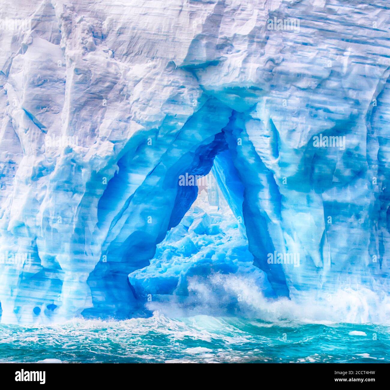 Wellen, die durch Bögen in schwimmenden Eisbergen in der Antarktis plätschern. Stockfoto