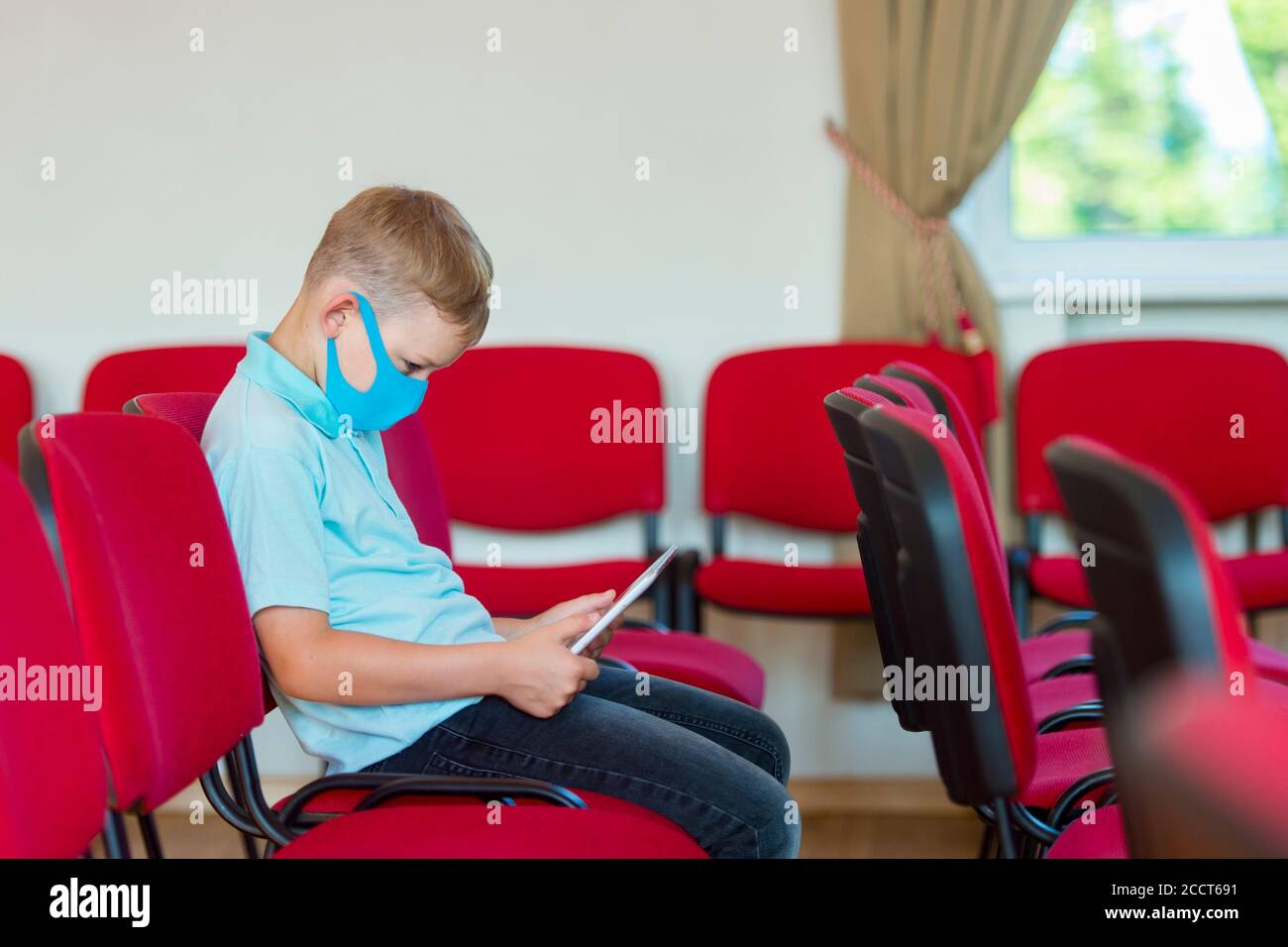 Schulkind mit blauer Maske gegen Virus und Tablet im Unterricht. Sicher zurück in die Schule während Pandemiekonzept. Soziale Distanzierung gegen COVID-19 Stockfoto