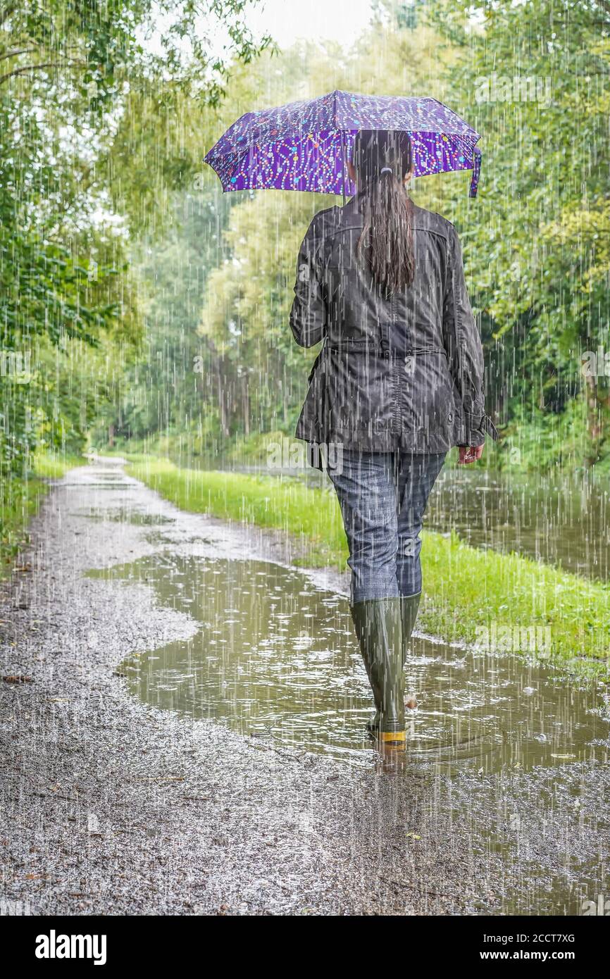 Frau von hinten trägt Gummistiefel mit Regenschirm, zu Fuß in Regenguss von schweren sintflutartigen regen isoliert, UK Kanal towpath. Britisches Sommerwetter! Stockfoto