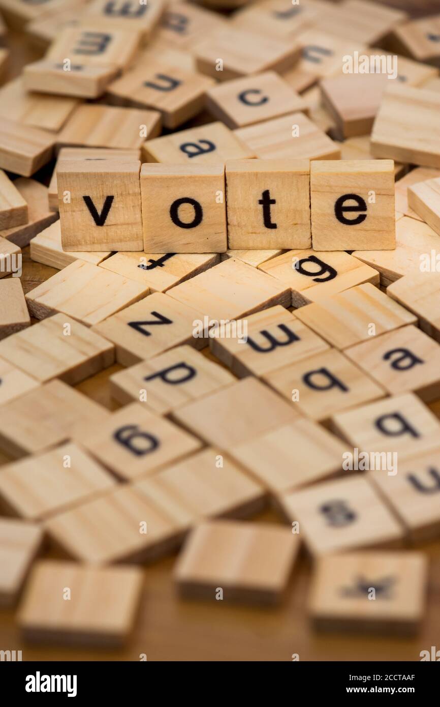 Holzbuchstaben, die das Wort "Abstimmung" auf einem Hintergrund von Verstreute Buchstaben verschüttet auf einem Holzbrett Stockfoto