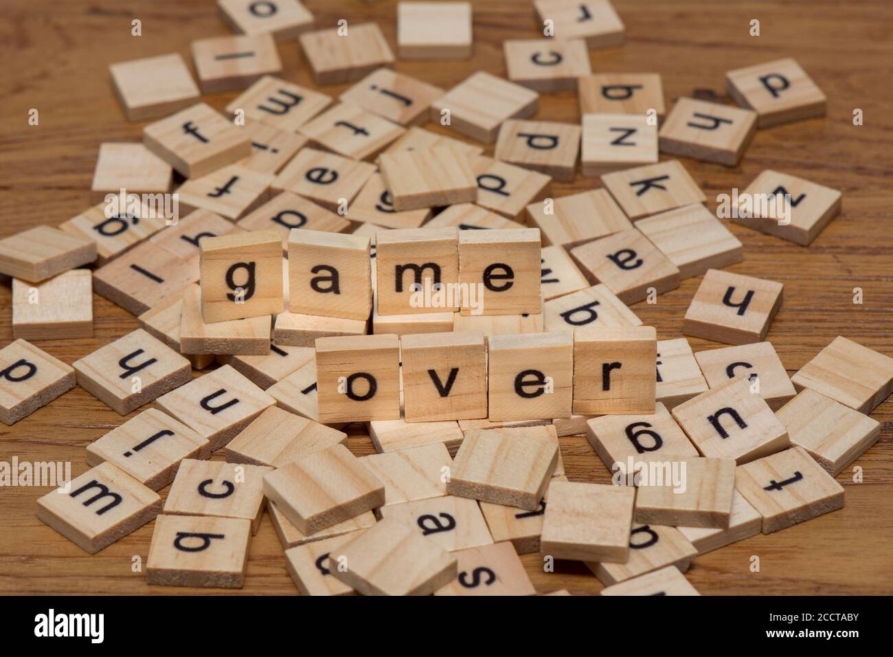 Hölzerne Buchstaben, die die Wörter "Spiel über" auf einem Hintergrund komponieren Von verstreuten Buchstaben verschüttet auf einem Holzbrett Stockfoto