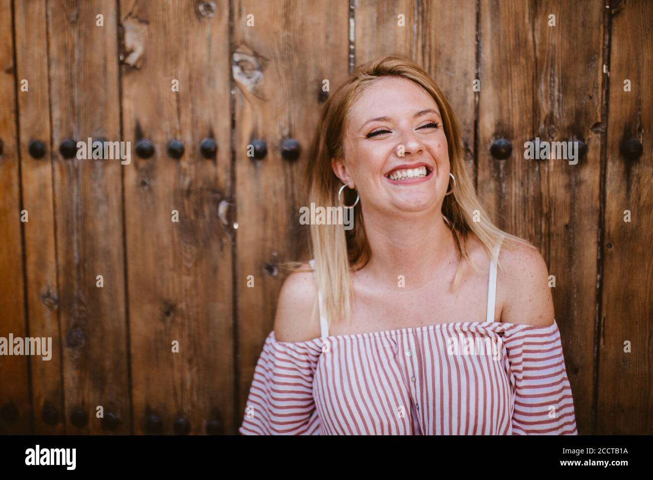 Blonde Frau lachend mit einem alten hölzernen Tür Hintergrund Stockfoto