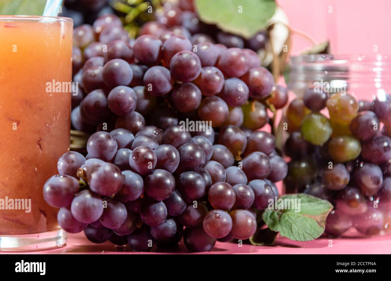 Topf mit Körnern und Traubentrauben. Traubensaft. Erfrischendes Getränk. Fruchtgetränk. Zutat für Weine und Säfte. Frisches Obst. Rosafarbene Traube. Stockfoto