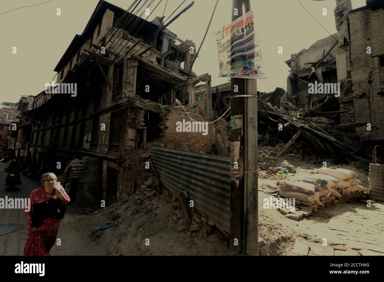 Eine ältere Bürgerin, die durch eine Wohnallee spaziert, in der Häuser durch die Erdbeben in Nepal 2015 in Bhaktapur, Bagmati Pradesh, Nepal, ruiniert wurden. Stockfoto