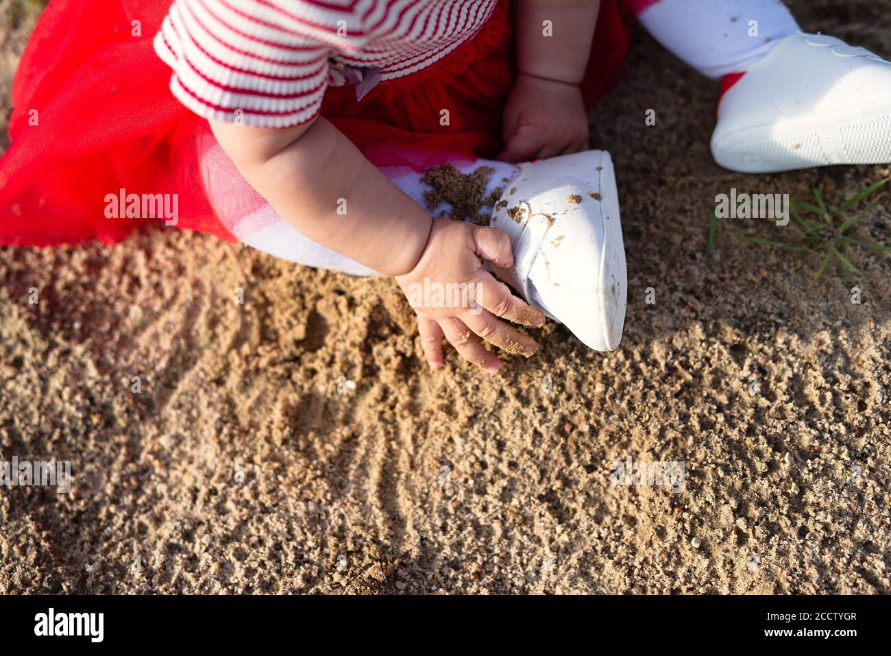 Kleines Mädchen in weißen Strumpfhosen und roten Kleid sitzt auf Sand, berühren Sand, Blick von oben Stockfoto