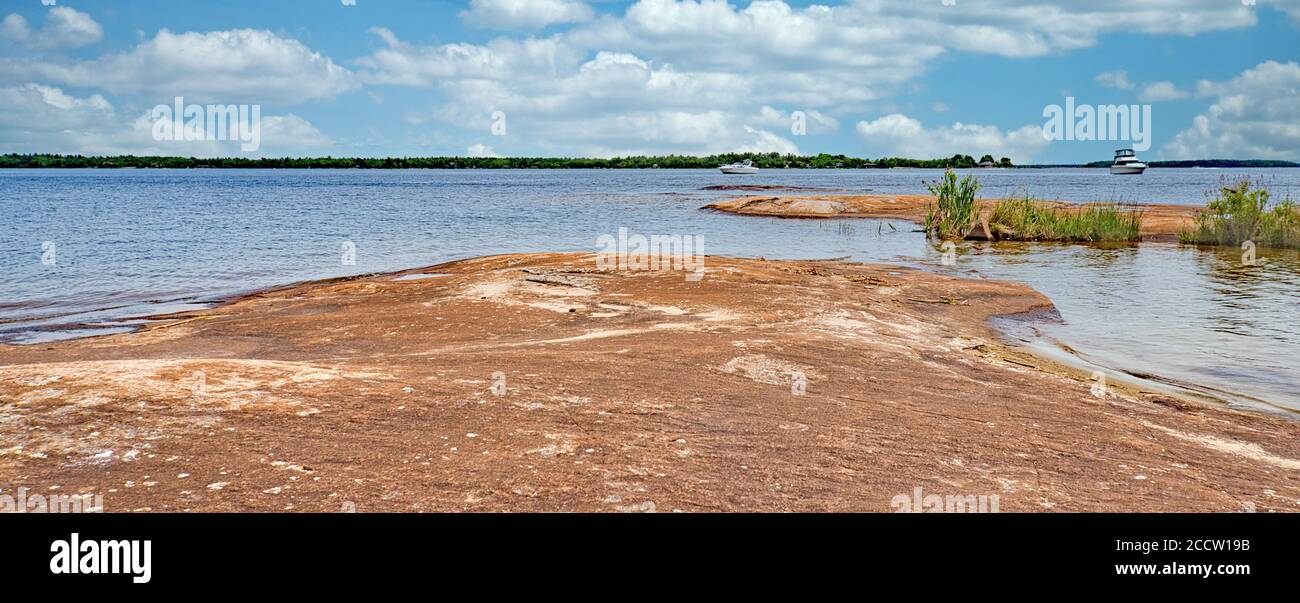 Sandsteinfelsenstrand im Georgian Bay Islands National Park mit Boote im Wasser unter weißen Wolken und blauem Himmel Stockfoto