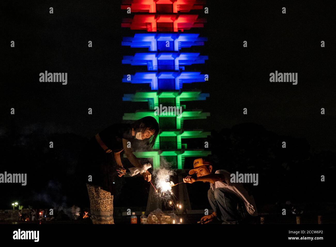 Tokio, Japan. August 2020. Ein Paar spielt Feuerwerkskörper vor dem Komazawa Park Olympics Memorial Tower ist in der Farbe der Paralympics beleuchtet, da es ein Jahr vor Tokio 2020 Paralympics geht. Die Paralympics und Olympischen Spiele 2020 in Tokio wurden aufgrund der COVID-19-Situation auf 2021 verschoben. Kredit: SOPA Images Limited/Alamy Live Nachrichten Stockfoto