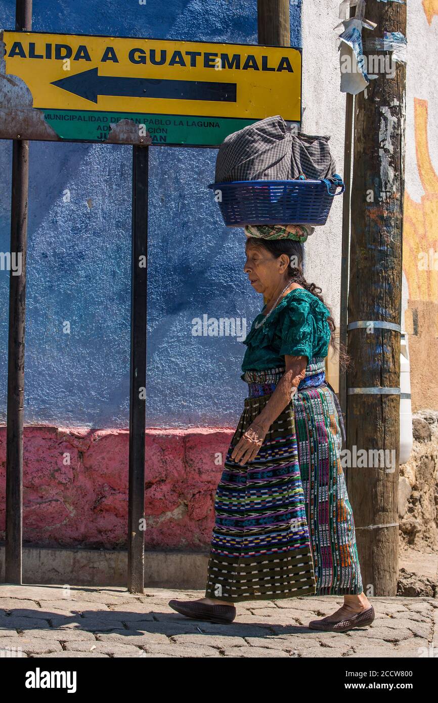 Eine ältere Tzutujil Maya Frau in traditioneller Kleidung gleicht ihre Last auf dem Kopf aus, als sie die Straße in San Pablo la Laguna, Guatemala, hinuntergeht. Beha Stockfoto