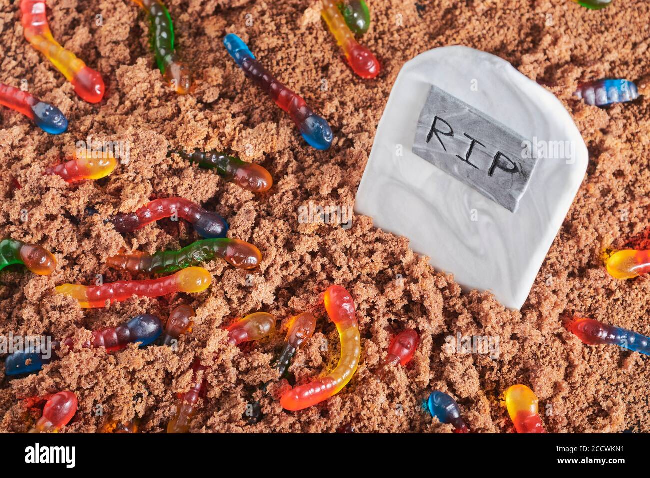 Bunt und hell sortiert Gummiwürmer in Schokoladenkuchen Boden um einen Zucker Grabstein, Halloween Party Essen Stockfoto