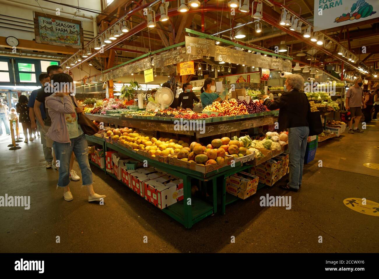 Menschen, die Schutzmasken tragen, kaufen Obst und Gemüse von einem Hersteller auf dem Granville Island Market, Vancouver, BC, Kanada Stockfoto
