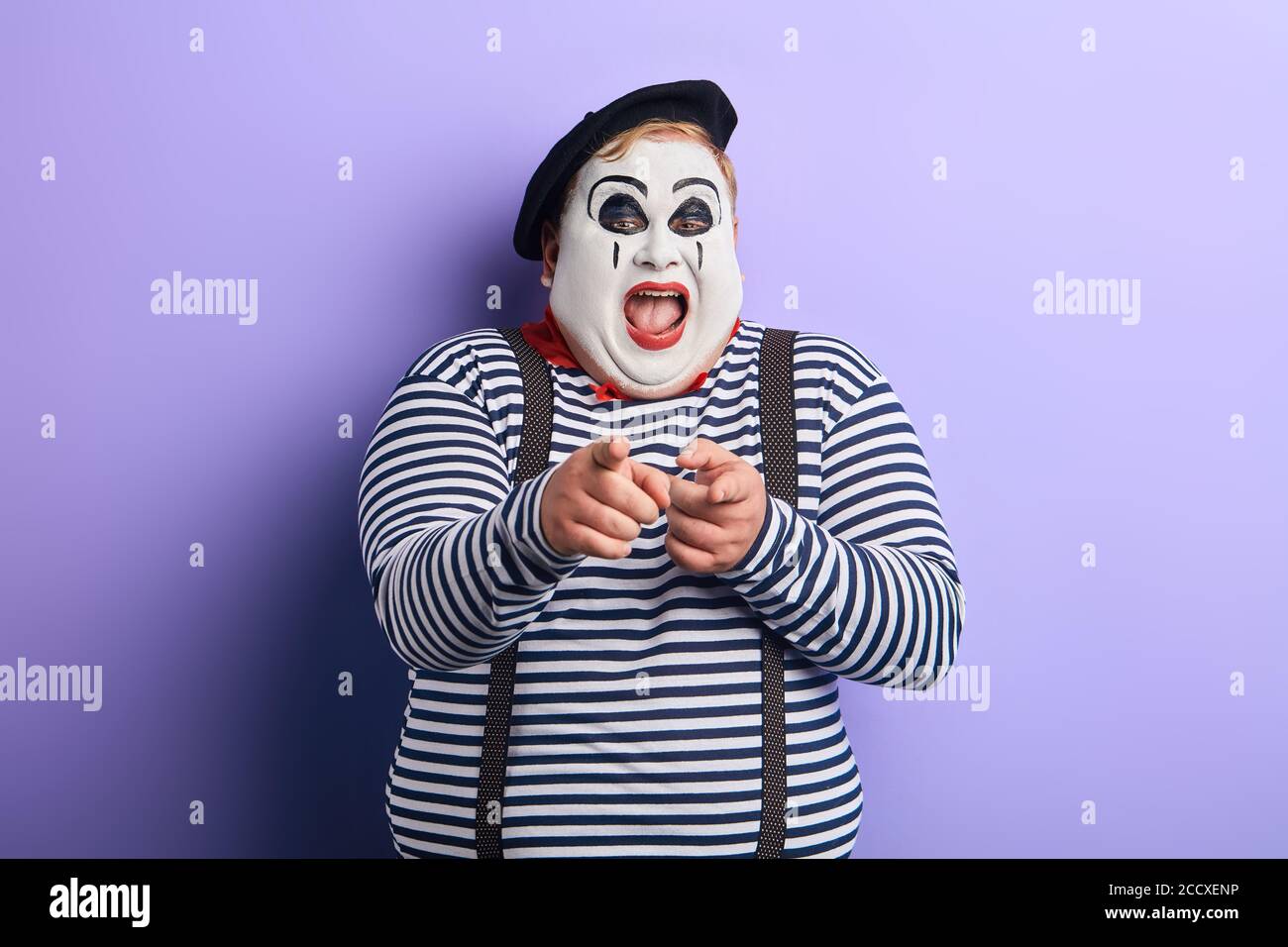 Künstler schüttelt Seiten mit Lachen, zeigt auf die Kamera, kichern. Isolierte blaue Hintergrund. studio-Aufnahme Stockfoto