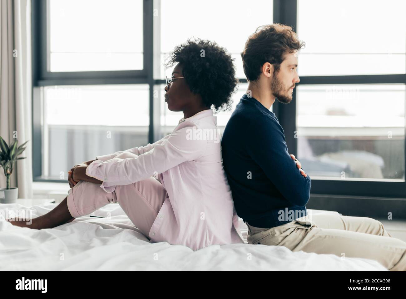 Zwei unglückliche gemischte Rasse Liebhaber nicht miteinander reden nach Streit während der Ferien zu Hause, sitzen auf dem Bett und sich gegenseitig ignorieren Stockfoto
