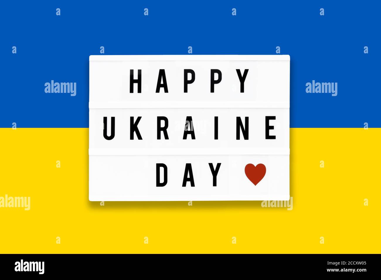 HAPPY UKRAINE TAG in einem Leuchtkasten auf einem Hintergrund der Ukraine Flagge Farbe geschrieben. Datum des Unabhängigkeitstages. Draufsicht Stockfoto