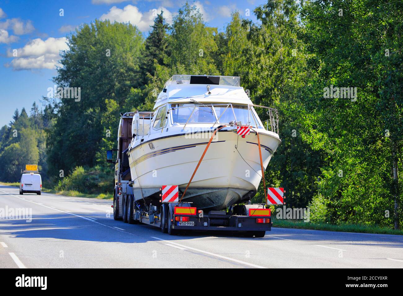 Pilotfahrzeug führt Überlasttransport eines Freizeitbootes auf der Autobahn 10. Tammela, Finnland. 21. August 2020. Stockfoto