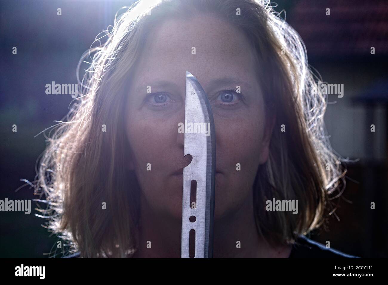 Porträt, geheimnisvolle Frau mit Messer vor ihrem Gesicht gegen das Licht, Horrorszene, Tatort, Deutschland Stockfoto