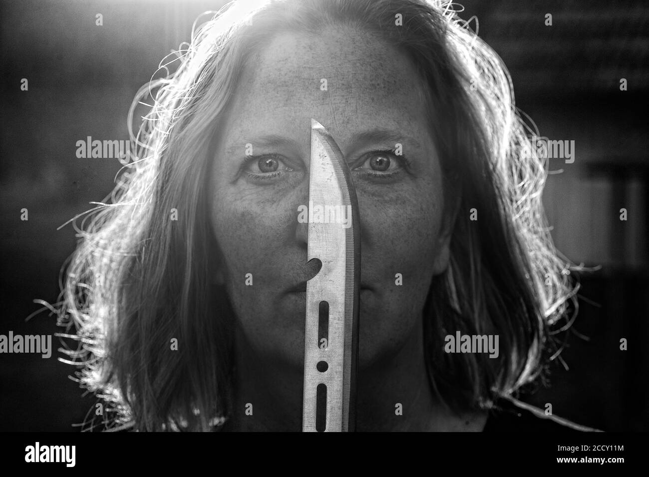 Porträt, geheimnisvolle Frau mit Messer vor ihrem Gesicht gegen das Licht, Horrorszene, Tatort, Deutschland Stockfoto