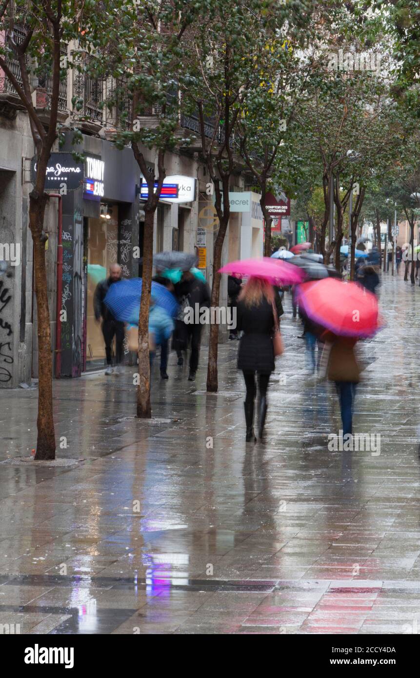Bewohner und Touristen gehen durch die berühmteste Fuencarral Straße, eine kommerzielle Straße nur für Fußgänger, voll von Geschäften und Lebensmittelgeschäften, auf einem regnerischen Stockfoto