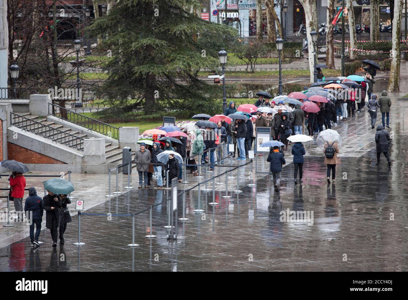 Touristen aus dem Ausland stehen mit ihren Schirmen an der Reihe Um ein Ticket für einen Besuch des Prado zu bekommen Museum an einem regnerischen sonntag in Madrid Stockfoto